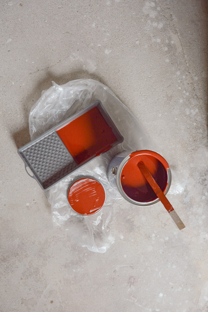 Foto von einem Farbeimer und Schale mit roter Farbe auf grauem Betonboden. 