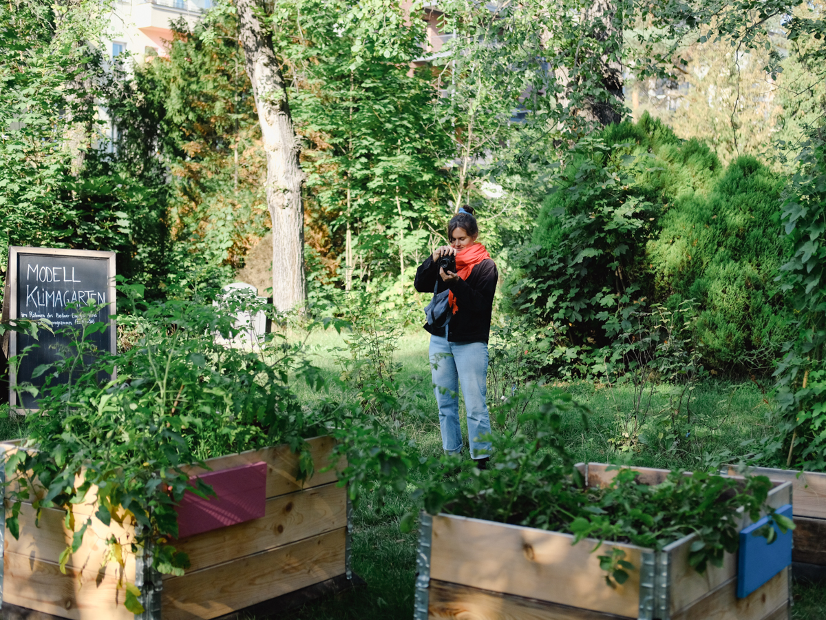 Person mit Kamera steht im Garten umgeben von Pflanzen und Natur.