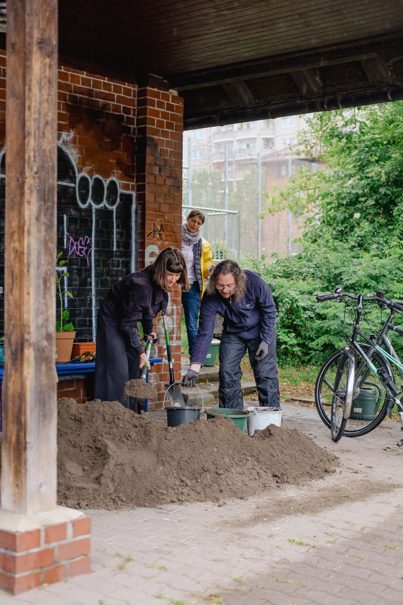 Zwei Personen schippen einen Erdhaufen in Eimer. 