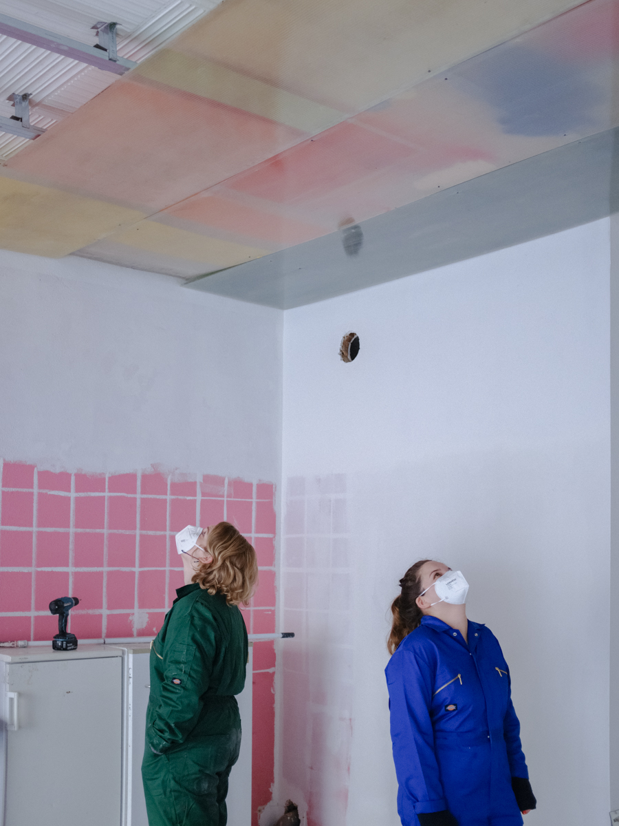 Personen in Arbeitsklamotten auf Baustelle im Innenraum betrachten Decke.