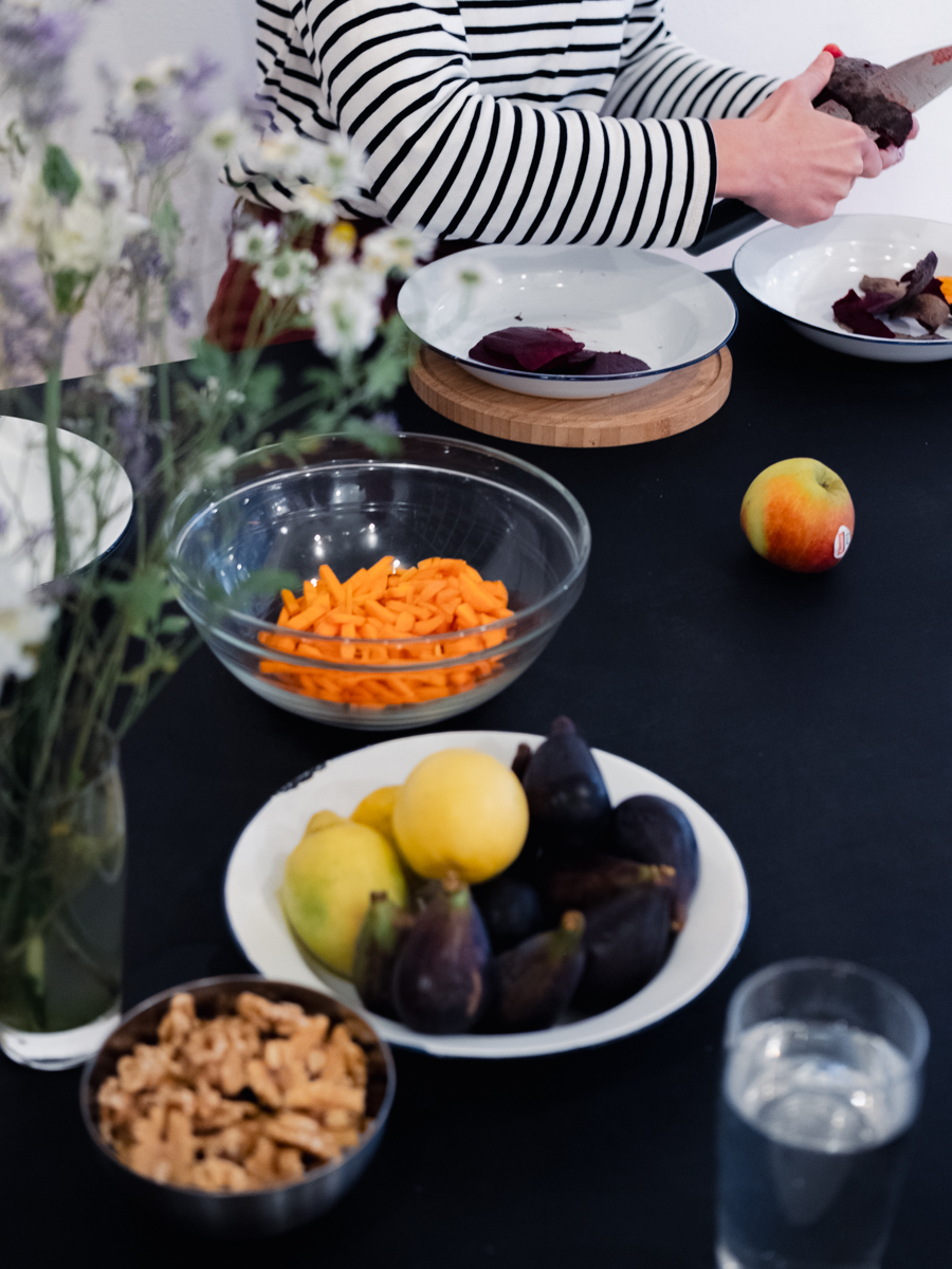 Nahaufnahme dunkler Tisch mit Tellern und Schüsseln, einer Blumenvase. Person schneidet Gemüse.