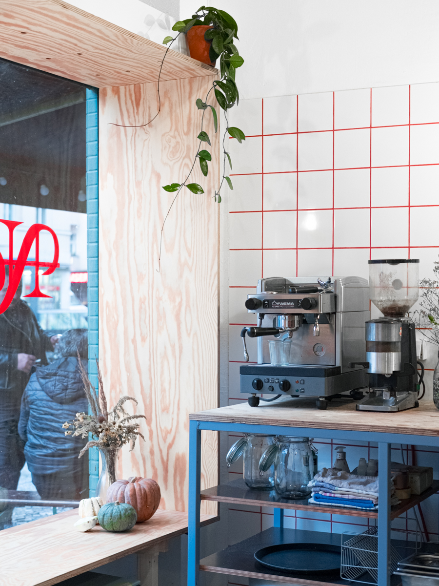Fensterrahmen aus Holz mit Küche im Vordergrund. Kaffeemaschine mit Küchenutensilien und Pflanze.